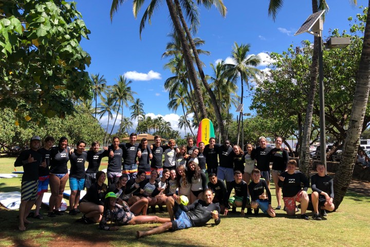 Group of people posing in a park with palm trees and surfboards.