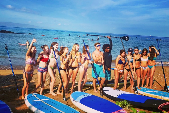 Group on beach with surfboards, smiling and posing with paddles.