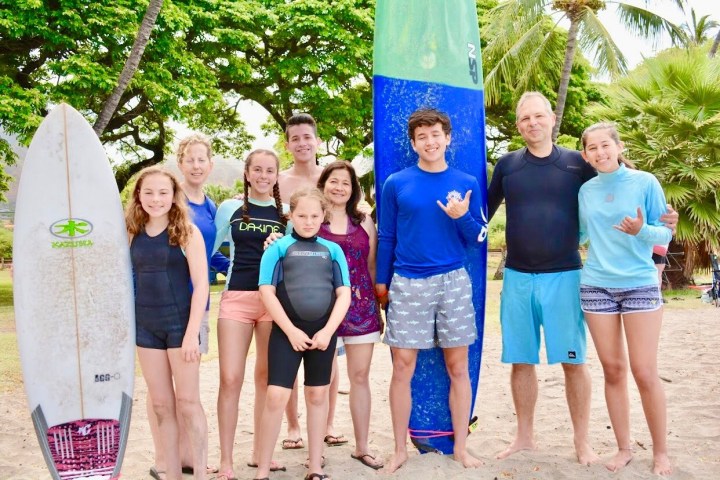 Group of nine people in swimwear posing with surfboards on a sandy beach.